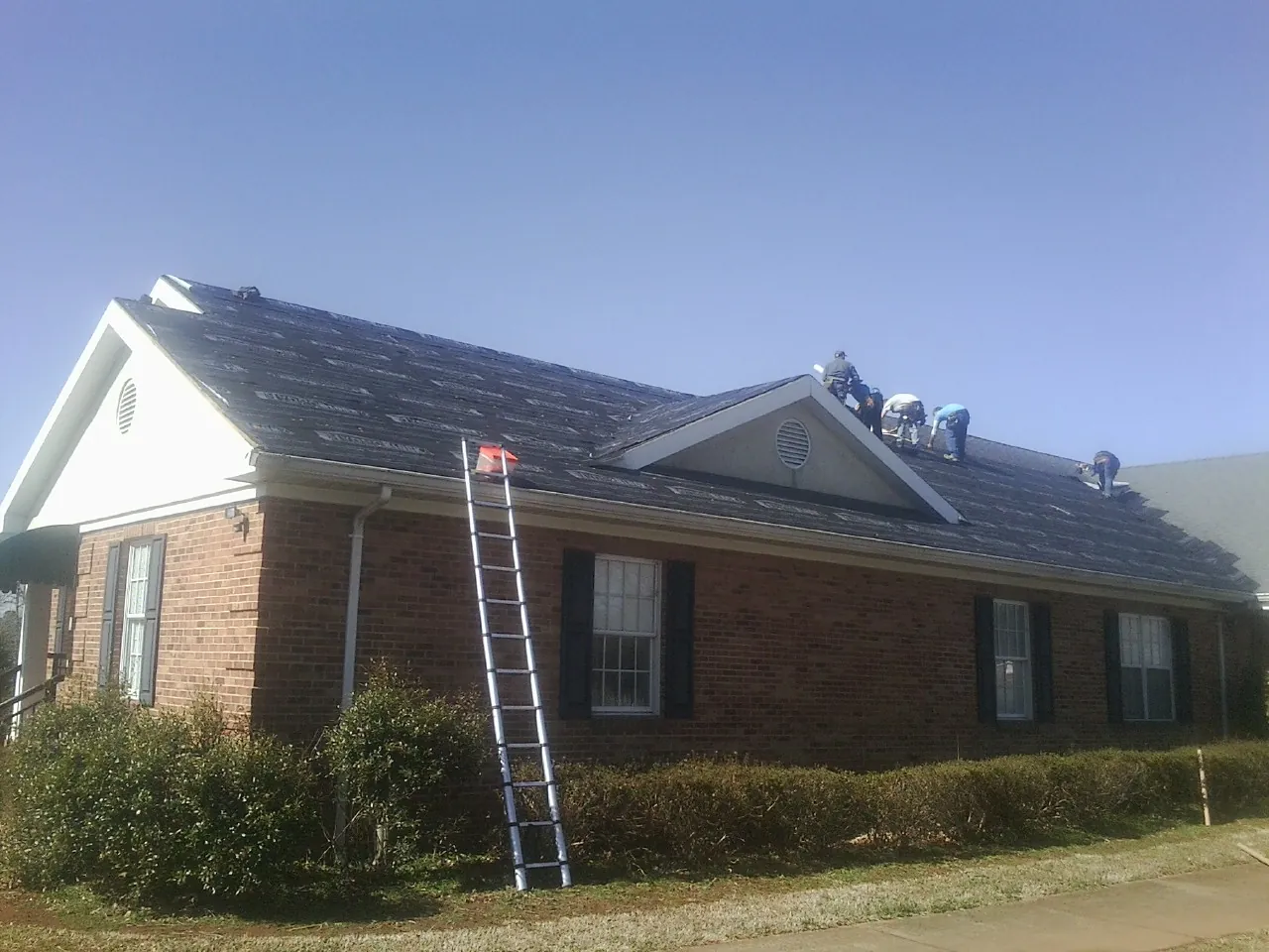 Crew tearing shingles off a brick ranch roof with a ladder set — Metal Roof Repair work by our crew in Newburyport