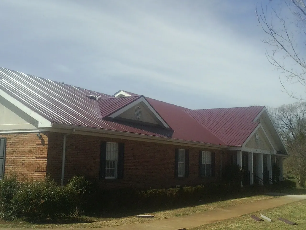 Red metal roof with gabled entries on a long brick building, from a Hail Damage Roof Repair job in Newburyport