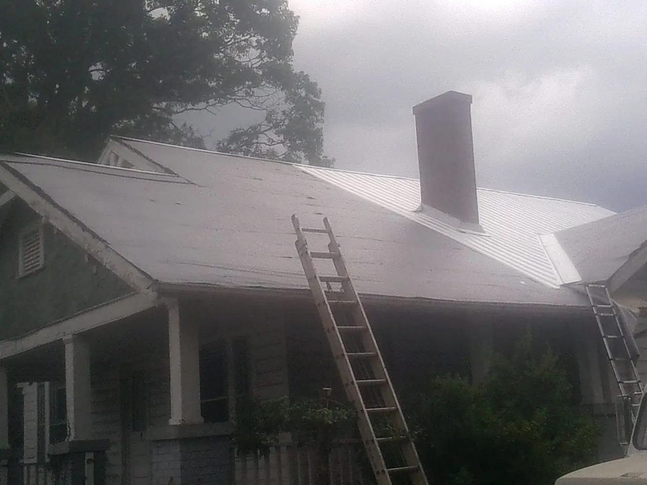 Ladders against a metal roof on an older home with a brick chimney in Newburyport