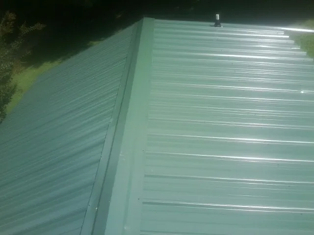 New green metal panels meeting at the ridge of a roof — Flat Roof Repair work by our crew in Newburyport