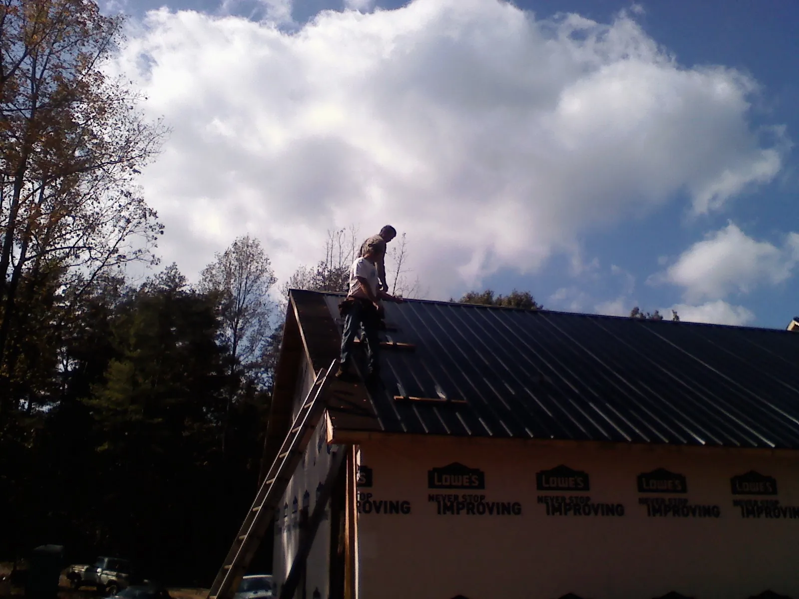 Roofer fastening dark metal panels high against a cloudy sky, from a Roof Inspection job in Newburyport