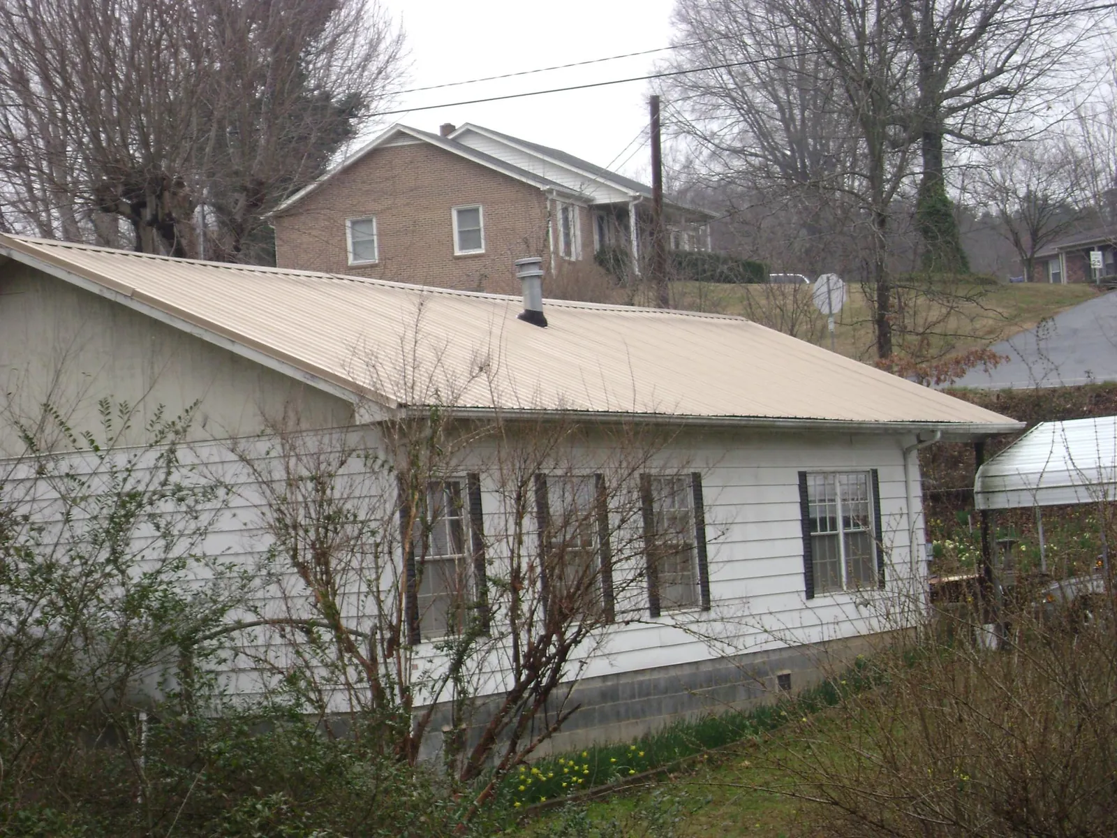 Tan metal roof on a white sided house set into a hillside — Commercial Roofing by Roofing Brothers in Newburyport